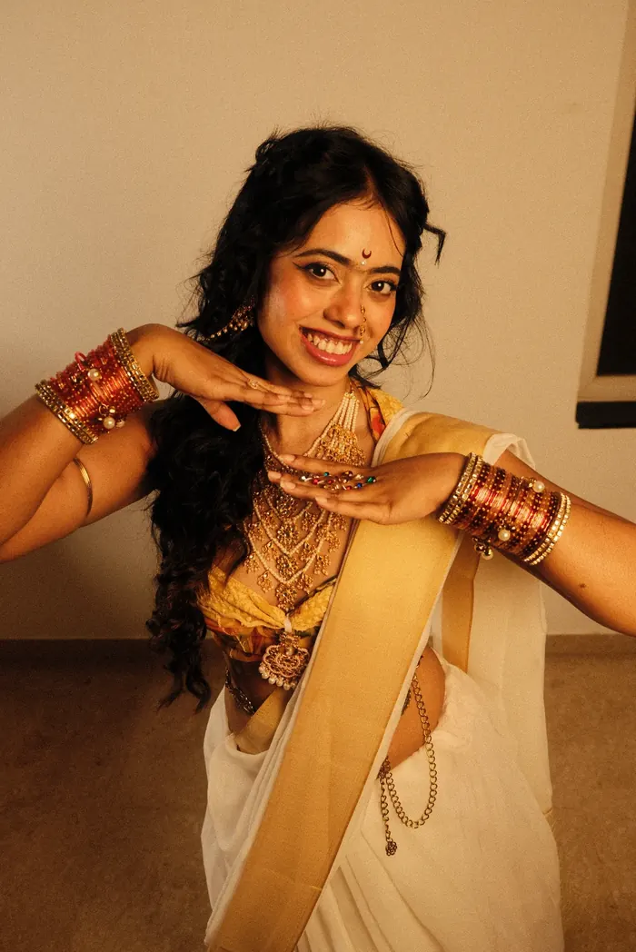 Sandipta in a cream sari and bangles, laughing mid-dance